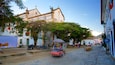 A cobblestone street lined with historic buildings, a church, and a colorful street vendor cart.