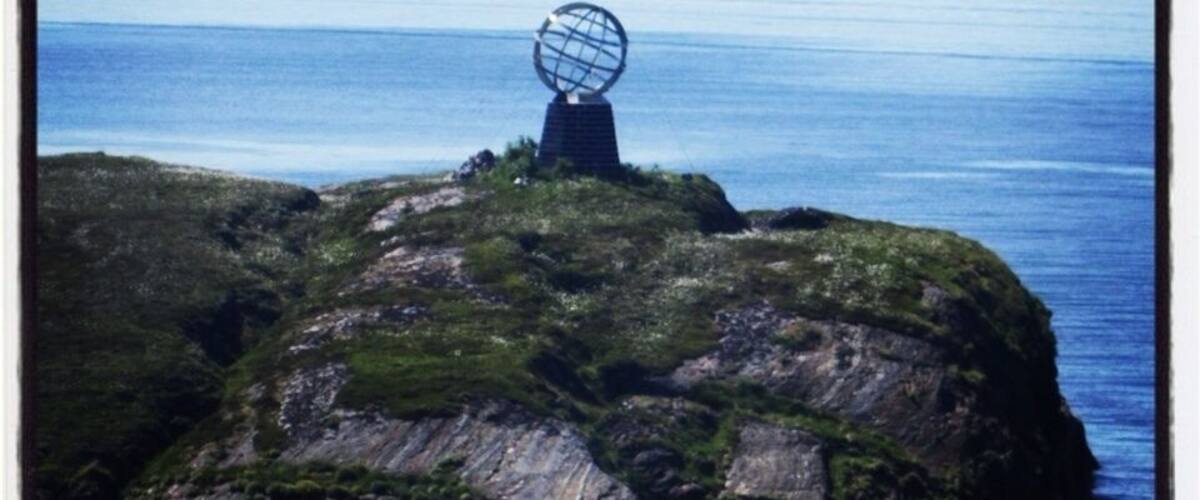 A rocky island with a spherical monument in the center, surrounded by calm blue waters and distant mountains.