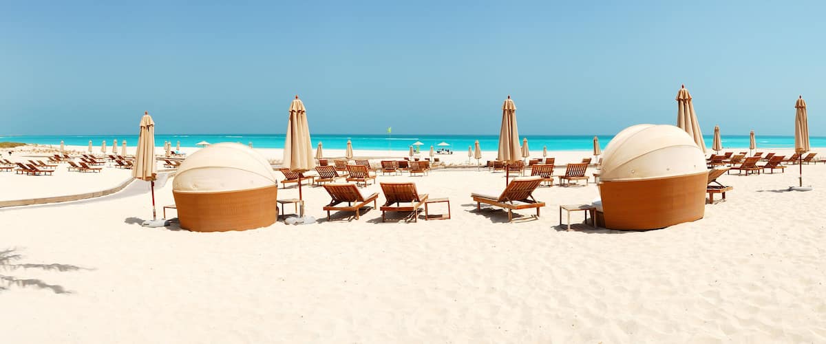 A beach with sun loungers, umbrellas, and large woven chairs.