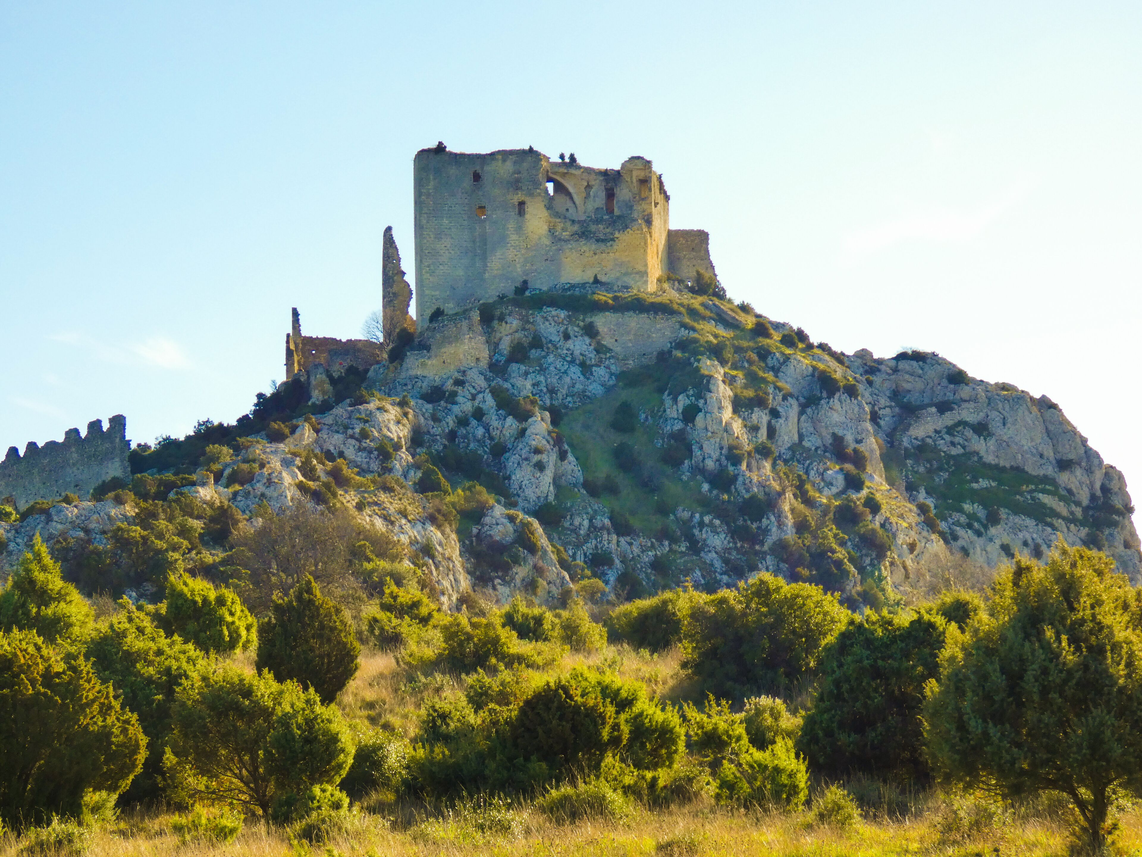A historic castle atop a rocky hill with lush greenery in the foreground.