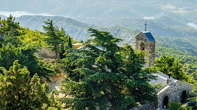 Una iglesia de piedra con un campanario rodeada por un bosque verde exuberante y un lago al fondo.