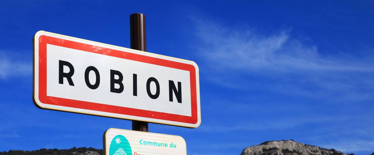A sign for 'Robion' and 'Commune du Parc naturel régional du Luberon' against a mountainous backdrop.
