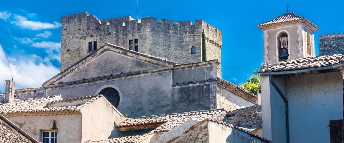 A historic stone castle with battlements, a bell tower, and traditional tiled roofs.