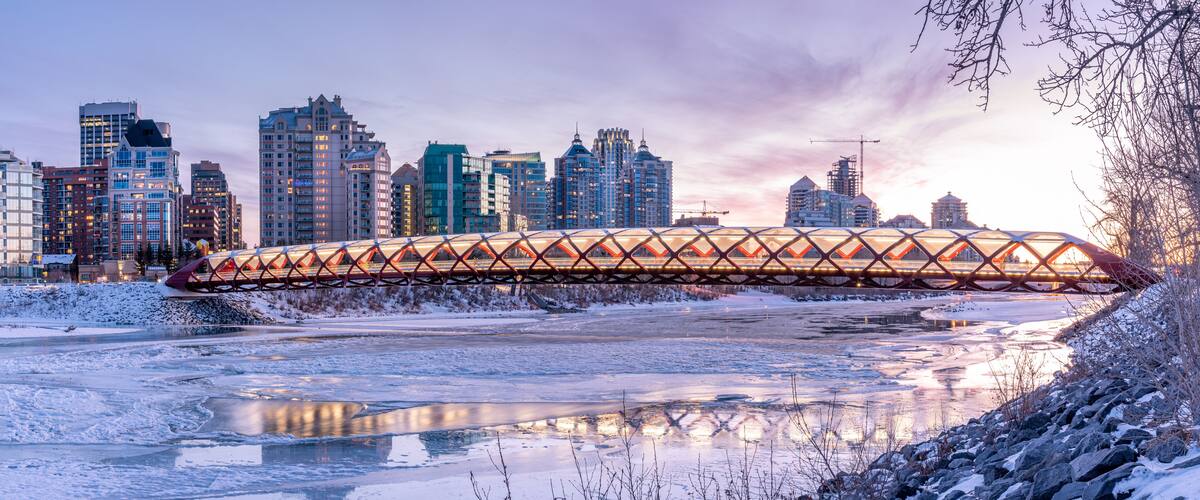 Un paisaje urbano con un puente distintivo sobre un río helado, rodeado de altos edificios y un paisaje nevado.
