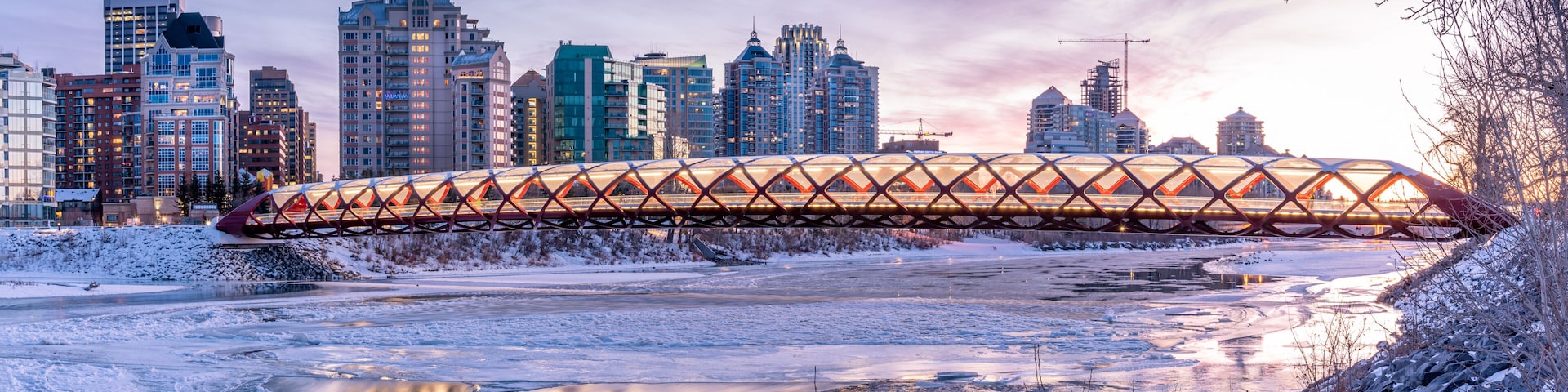 A cityscape with a distinctive bridge over a frozen river, surrounded by tall buildings and a snowy landscape.
