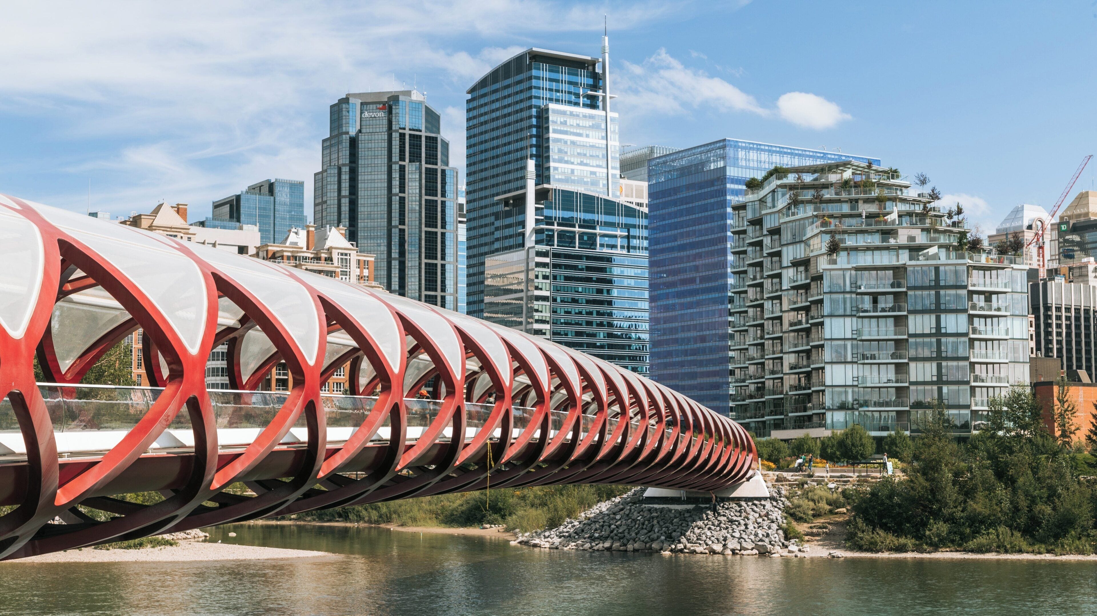 Beautiful day at Peace Bridge on Bow Riverfront in Calgary, Alberta, showcasing modern architecture alongside serene waterways and urban life