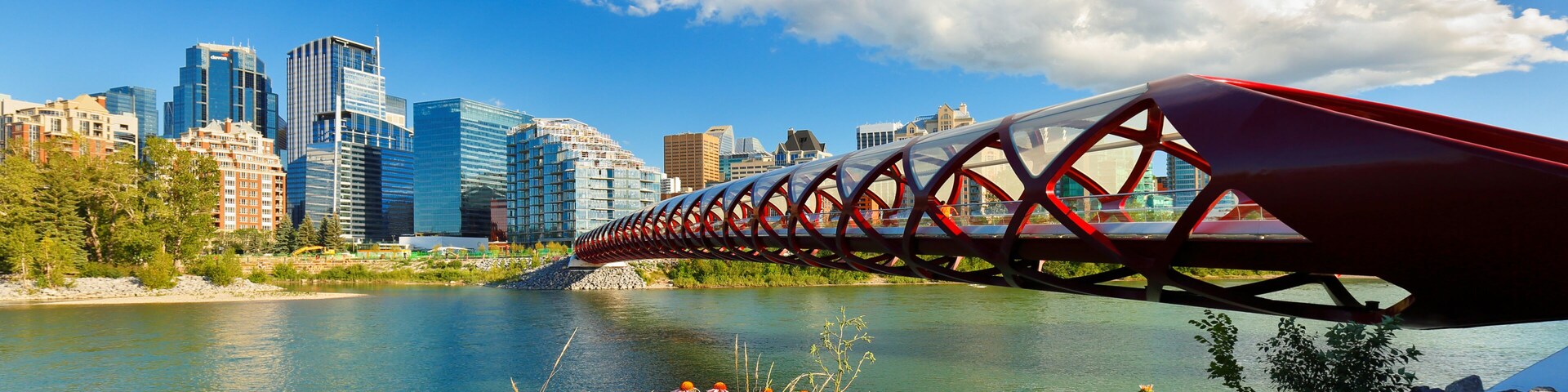 Un puente rojo sobre un río con el horizonte de una ciudad al fondo.