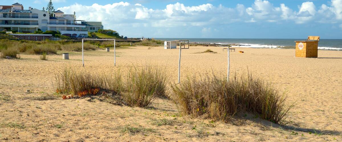 A sandy beach with a lifeguard tower, a wooden hut, and a building with a balcony overlooking the ocean.