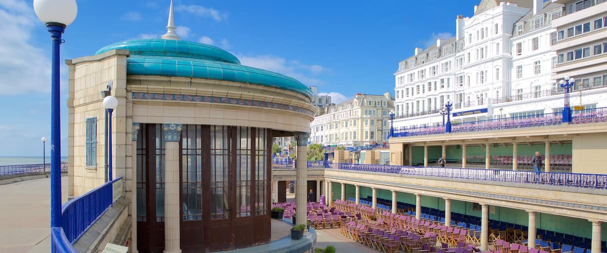 A seaside promenade with a covered seating area, a blue-domed building, and a hotel with balconies.