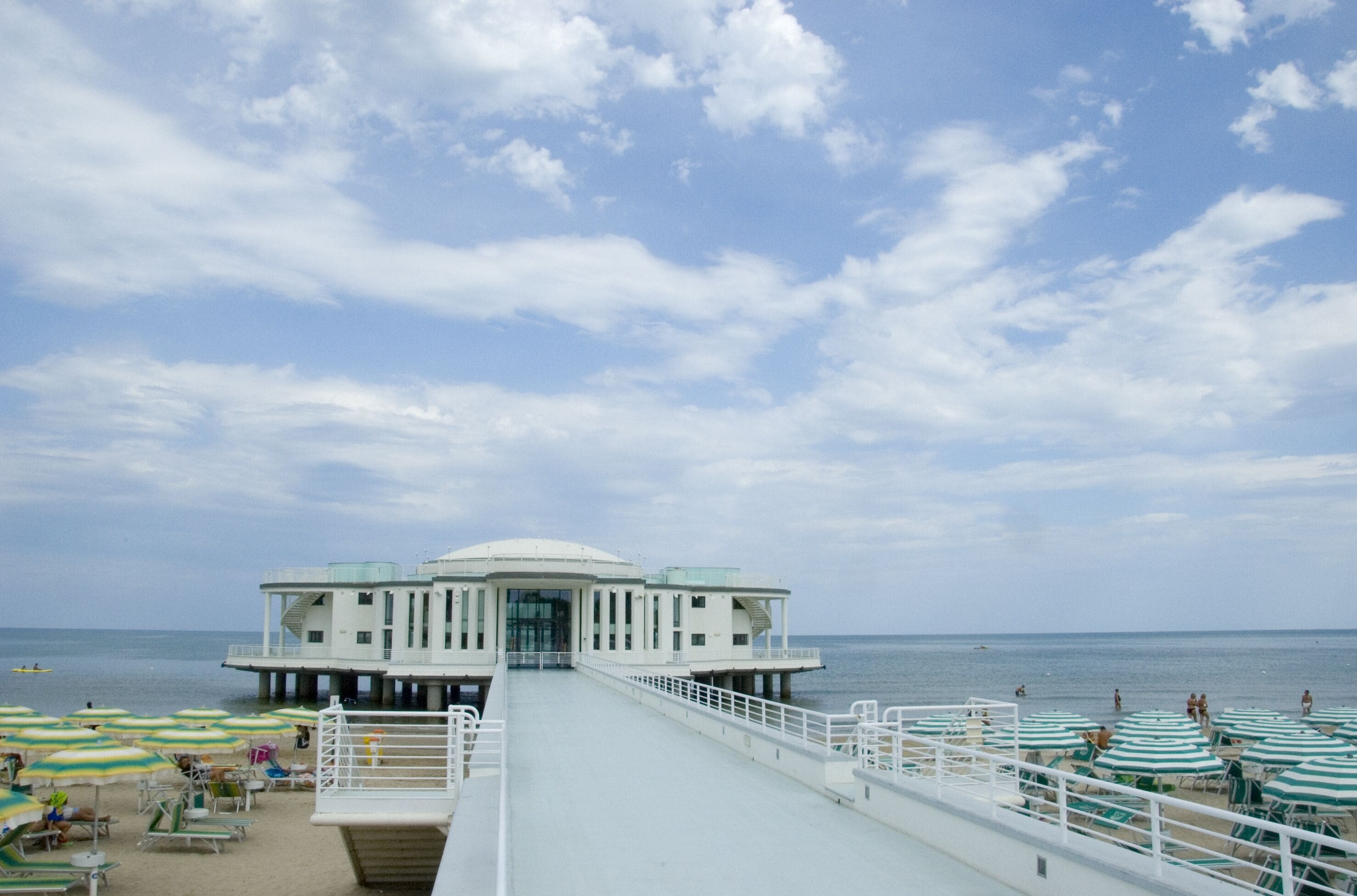 The walkway to the Rotonda a Mare with rows of umbrellas on either side in Senigallia, Marche, Ancona, Italy, complete with a sunny beach, blue sky and fluffy clouds