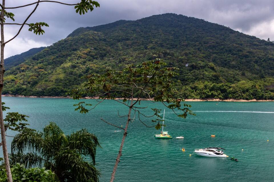 Paisagem costeira com montanha, águas turquesa cristalinas e vários barcos.