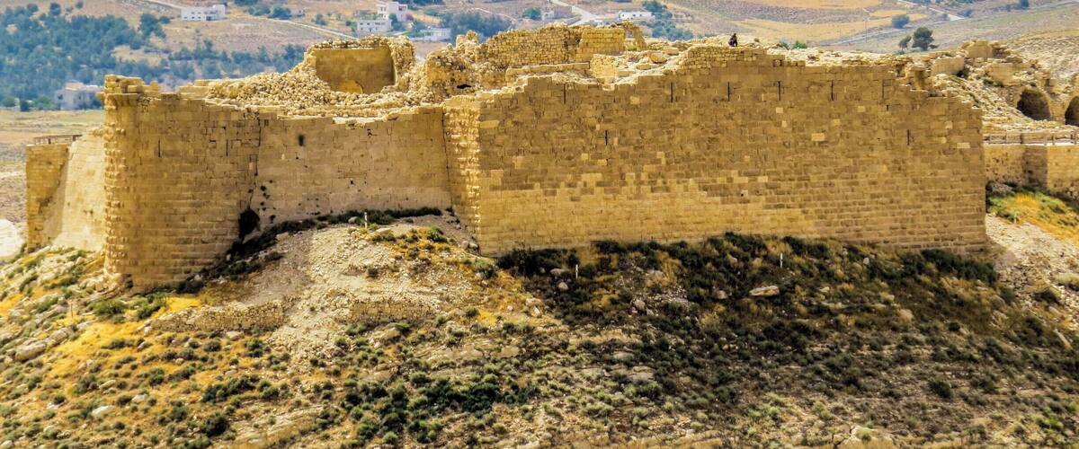 Een historisch stenen fort met ruïnes en een heuvellandschap op de achtergrond.