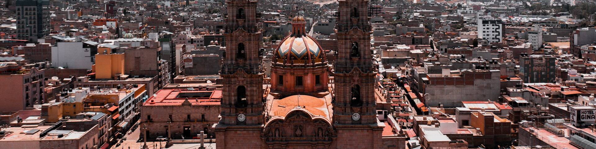 A historic cathedral with two towers and a dome, surrounded by a densely packed cityscape.