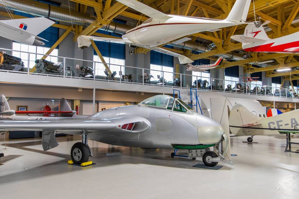 A silver airplane with a green tail fin and registration number CE-AZM in a museum hangar.
