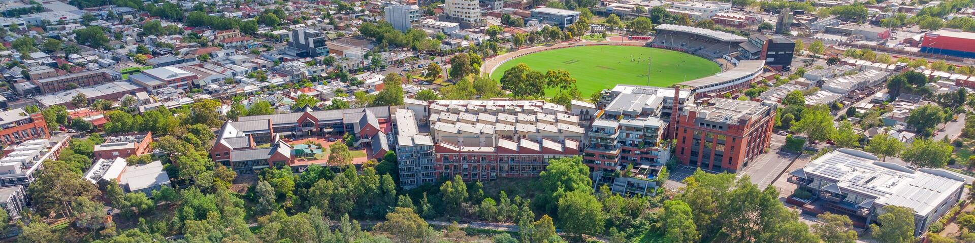 Aerial view of a river and waterfall bordered by city buildings along side and bush