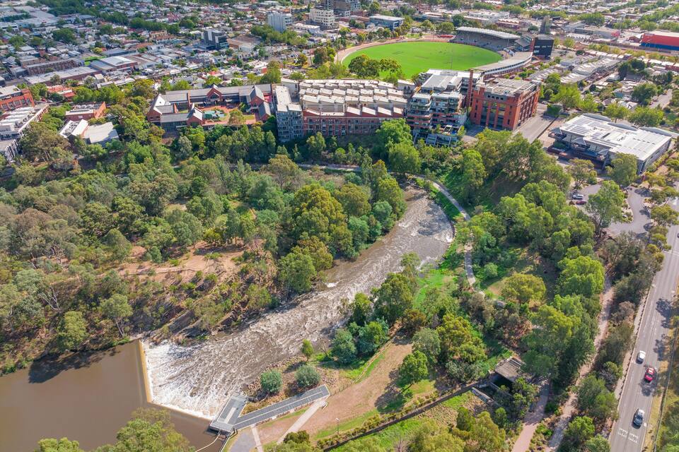 Vista aérea de una ciudad con un río, zonas verdes y un estadio.
