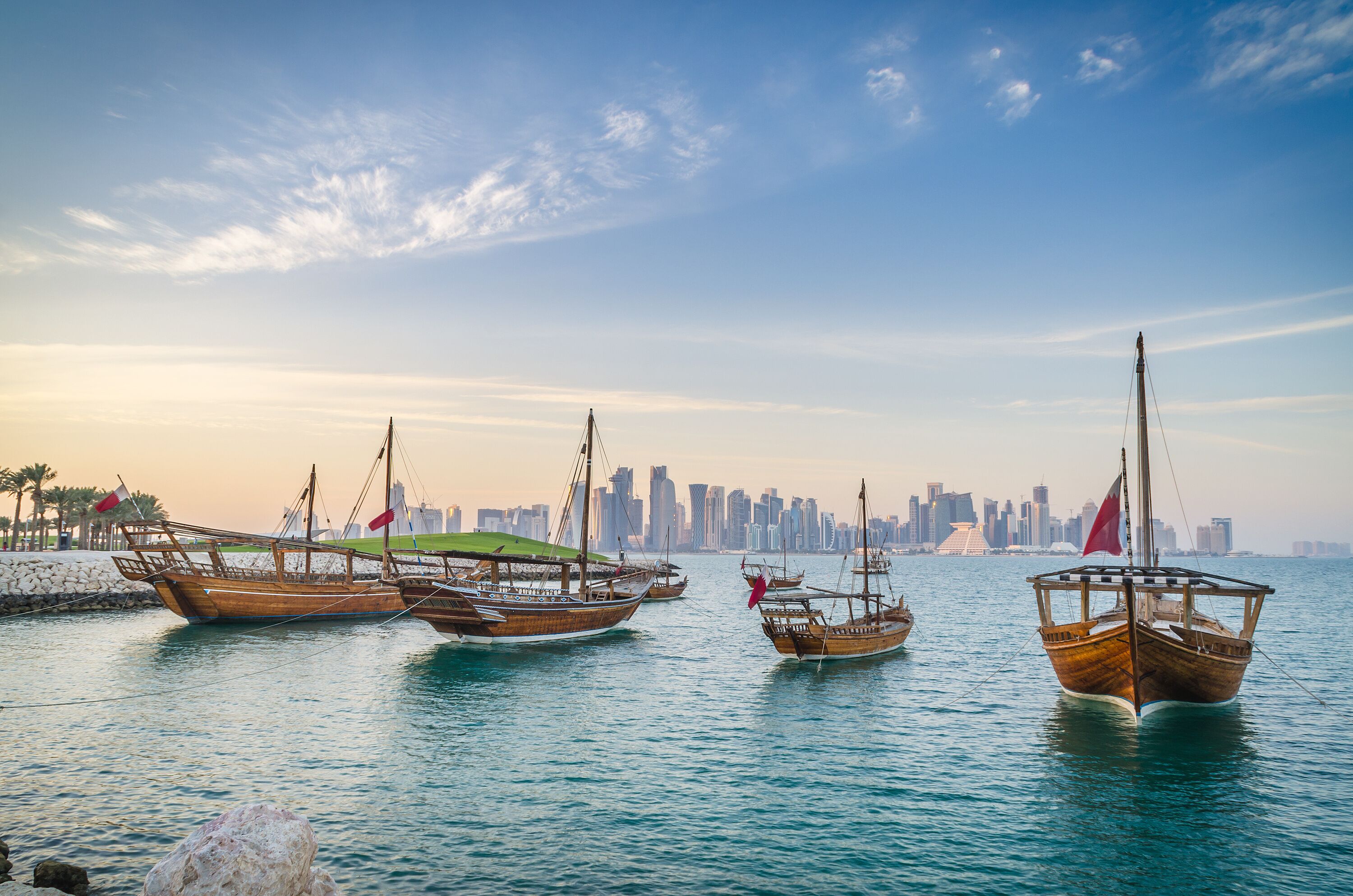 Barcos de madera tradicionales amarrados en una orilla con el horizonte de una ciudad al fondo.
