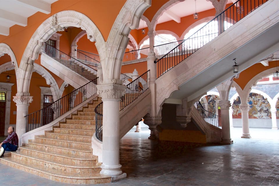 Una gran escalera con columnas blancas ornamentadas y una pared naranja brillante.