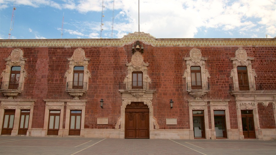 Un edificio histórico con balcones ornamentales, grandes puertas de madera y un friso decorativo.