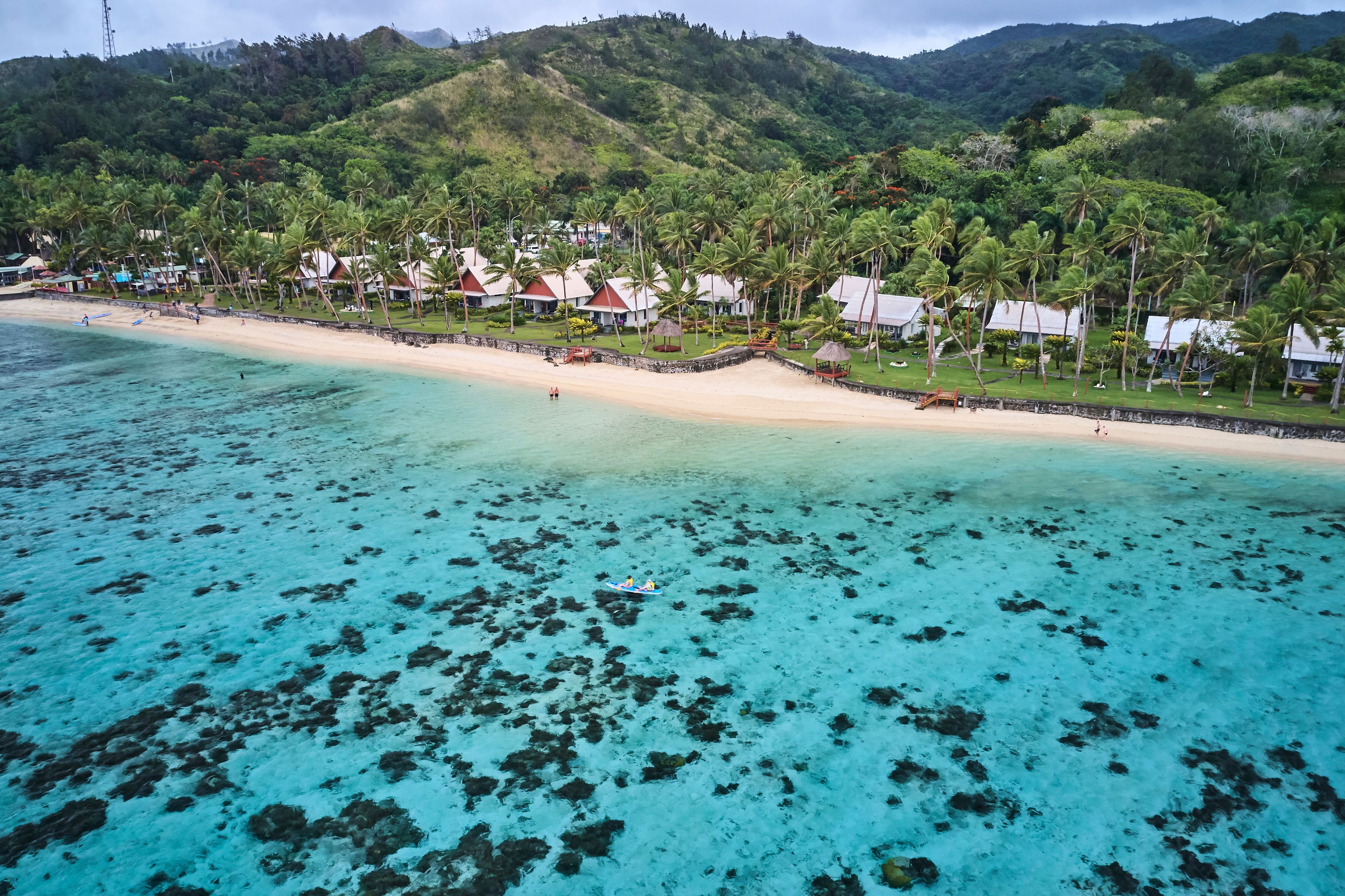 A tropical beach with clear turquoise waters, palm trees, and resort buildings.