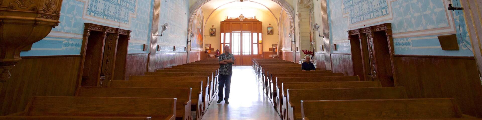 An ornate church interior with blue patterned walls, wooden pews, and a central altar.