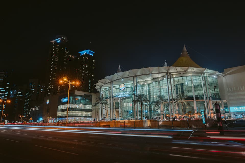 Un edificio moderno con fachada de vidrio y una cúpula distintiva, rodeado de rascacielos y palmeras.