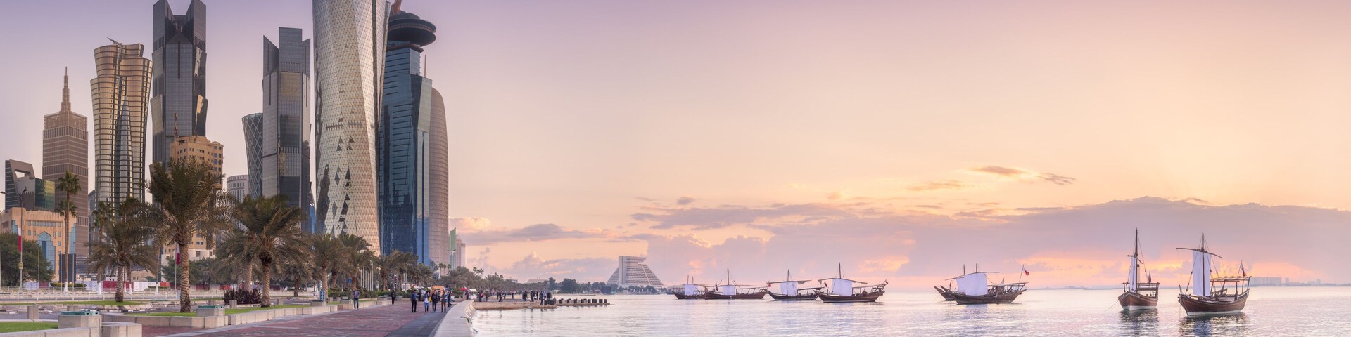 Paisaje urbano frente al agua con rascacielos modernos y barcos tradicionales.