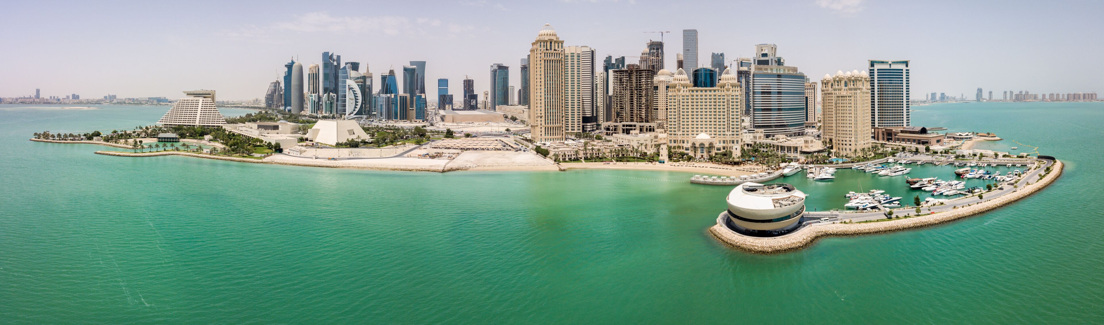 The skyline of Doha, Qatar. Modern rich middle eastern city of skyscrapers, aerial view in good weather, midday, during hot dry summer, with view of marina and beach of Persian Gulf/Arabian Gulf
