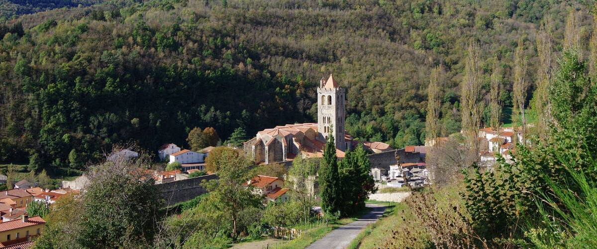 A village with a prominent church featuring a tall bell tower, surrounded by lush green hills and a clear blue sky.