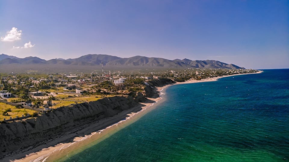 A coastal town with a beach, mountains, and clear blue waters.
