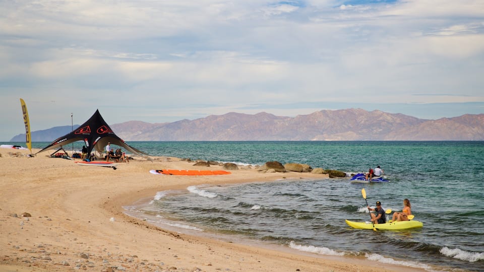 A beach with a tent, kayaks, and mountains in the background.