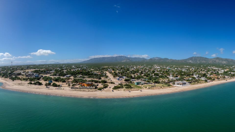 An aerial view of a coastal town with a beach, houses, and mountains in the background.