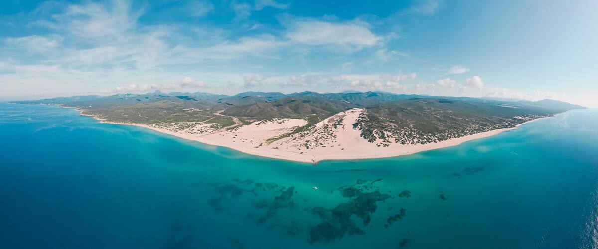 A coastal island with a sandy beach, clear turquoise waters, and a mountainous backdrop.
