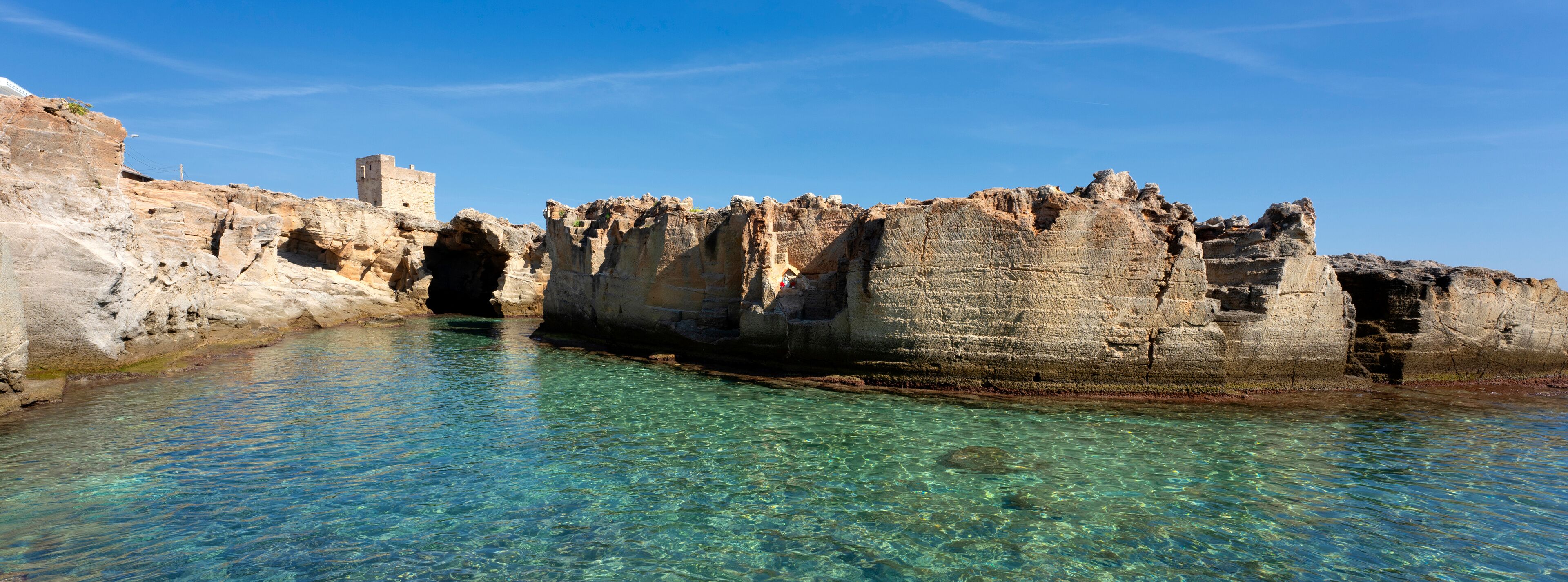 A coastal cave formation with clear water and a small tower structure.