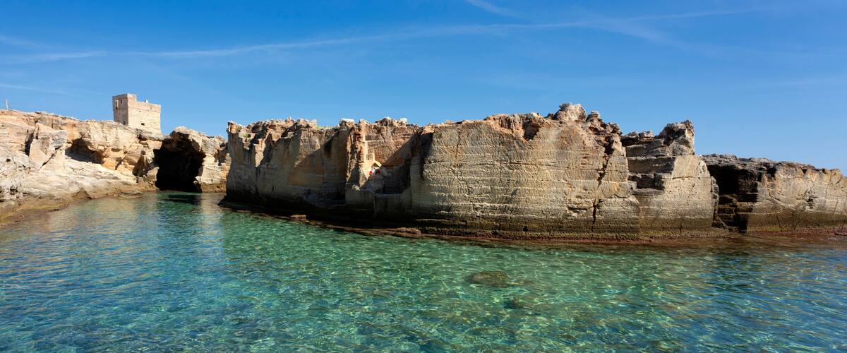 A coastal cave formation with clear water and a small tower structure.