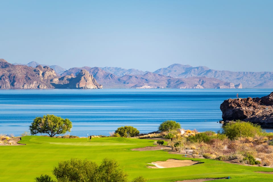 Un campo de golf con vistas despejadas al océano y montañas al fondo.
