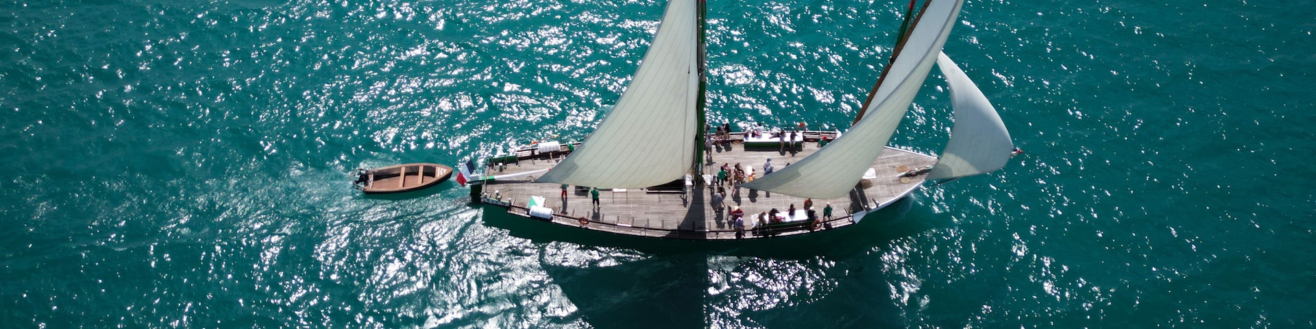 Yvoire, France - 27 July 2024: Aerial view of a traditional sailing boat cutting through the turquoise waters of Lake Geneva, sails billowing in the wind, reflecting the sunlight.
