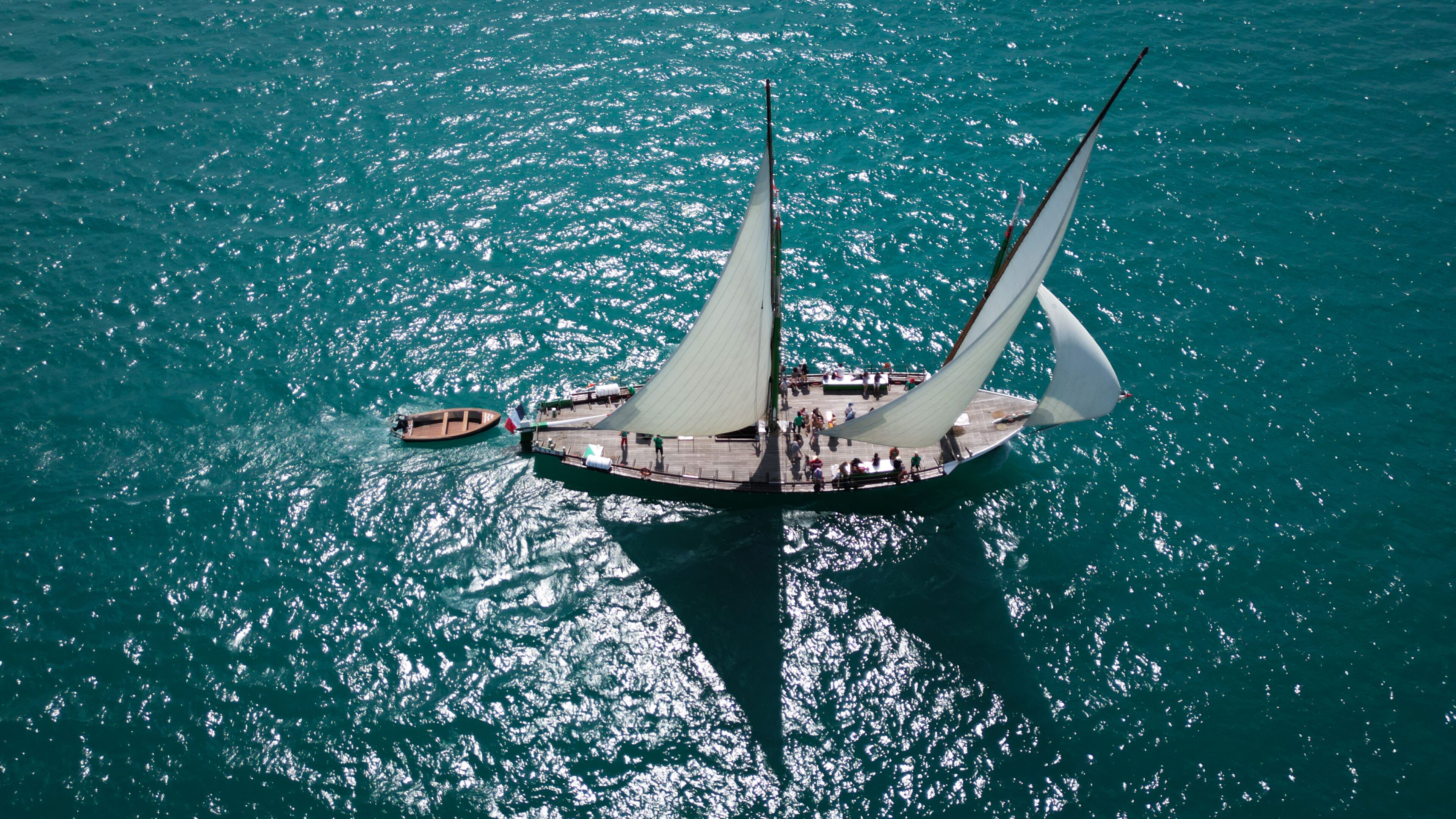 A large sailboat with multiple sails on a turquoise sea.