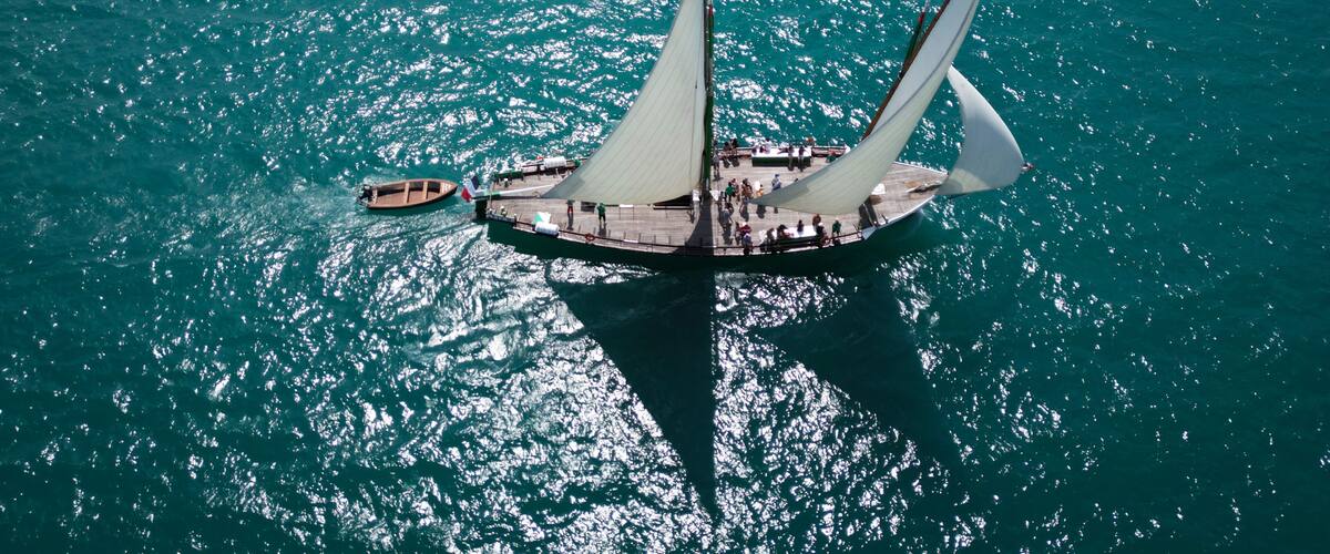 A large sailboat with multiple sails on a turquoise sea.