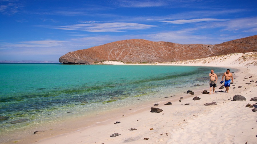 Une plage bordée d’une eau turquoise et limpide, d’un rivage rocheux et dominée par un paysage montagneux.