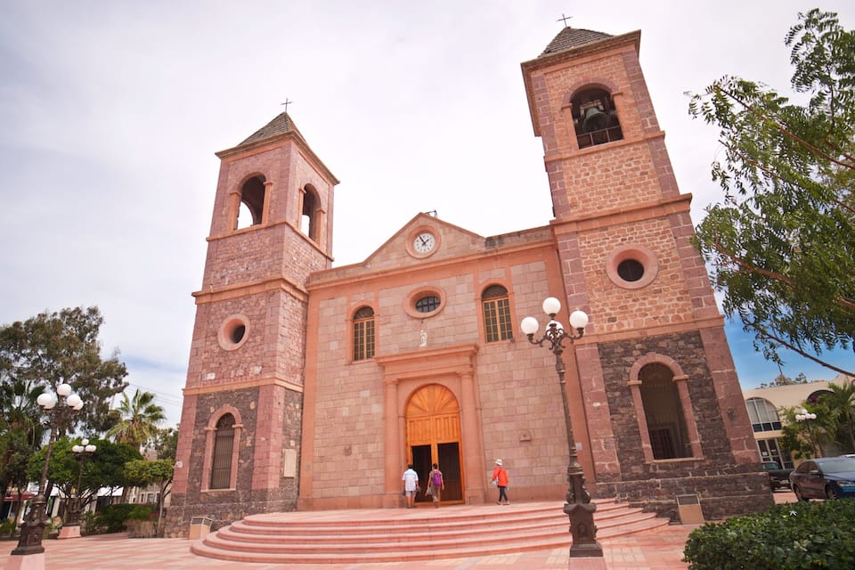 A historic church with two bell towers, a large central doorway, and a clock.