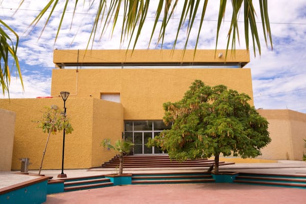 Um edifício com fachada amarela, uma árvore em frente e céu claro.