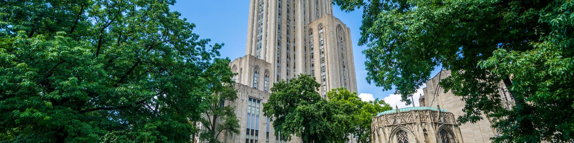A historic building with a tall tower, surrounded by lush green trees and a well-maintained lawn.