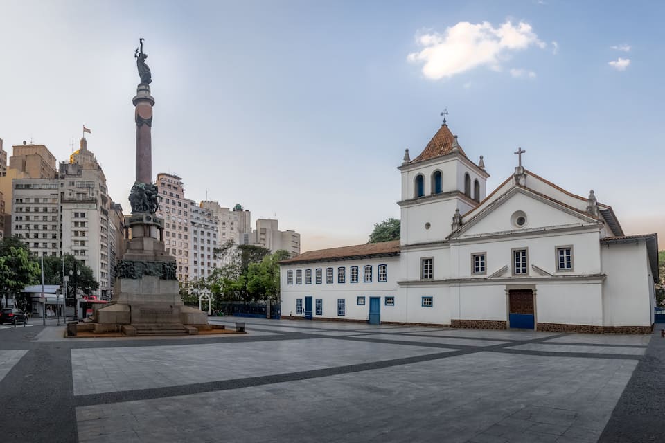 A plaza with a monument, a church, and surrounding buildings.