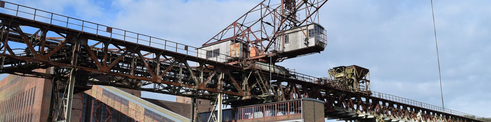 A large industrial crane, a brick building, and a grassy area.