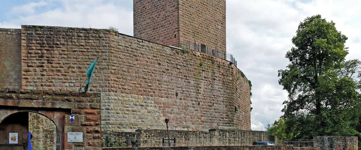 A historic brick tower with a flag, a gate, and a tree in the background.