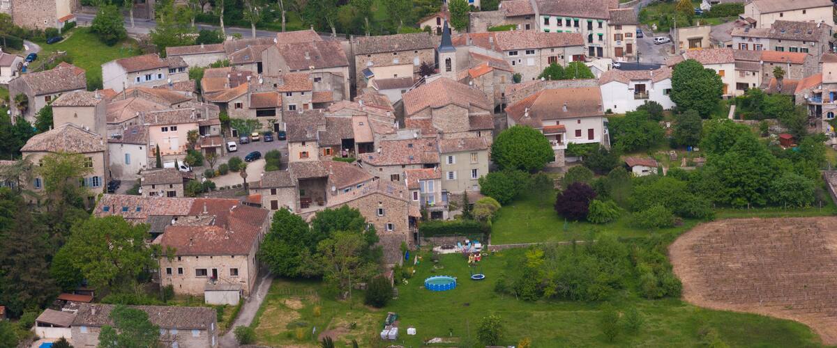 A densely packed village with terracotta-roofed buildings, surrounded by lush greenery and agricultural fields.