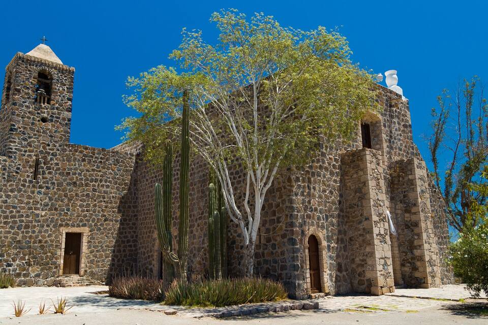 Une église historique en pierre, dotée d’un clocher et agrémentée de cactus.