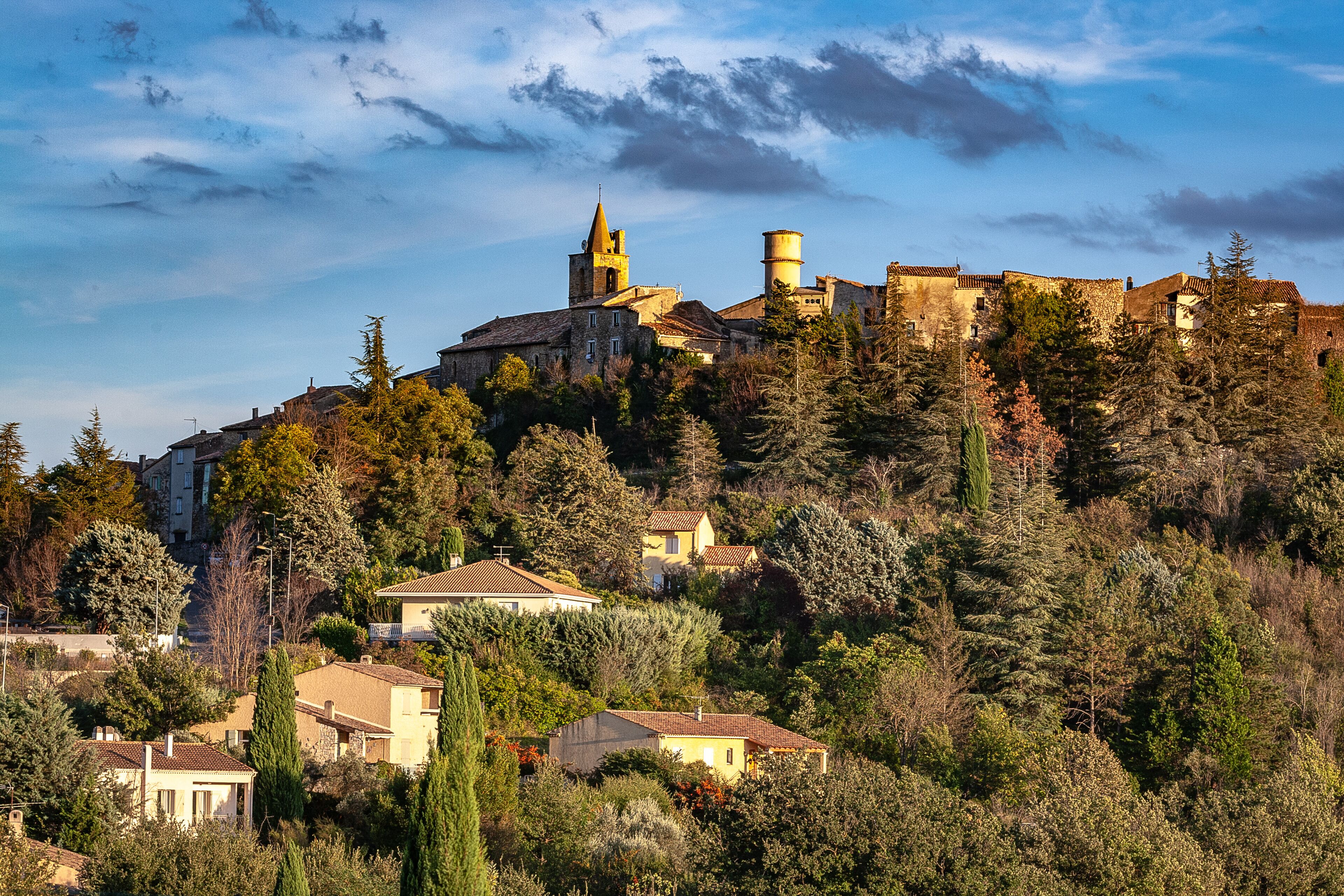 A historic hilltop town with a prominent church and bell tower, surrounded by dense trees and residential buildings.