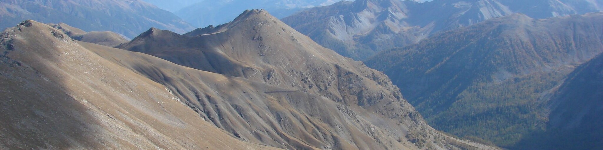 Paisaje montañoso con terreno accidentado y cumbres lejanas bajo un cielo despejado.
